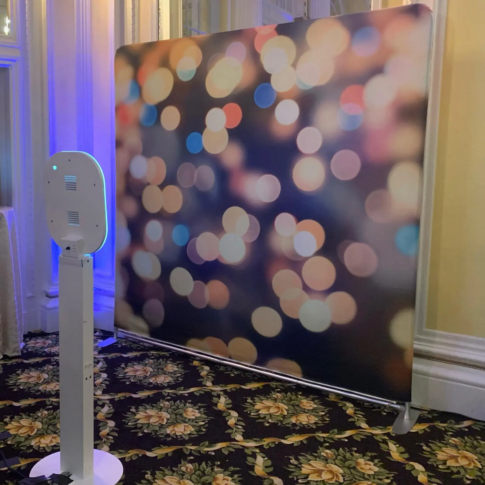 Photobooth Rental Michigan setup featuring a sleek white stand and festive bokeh backdrop in an elegant event venue.