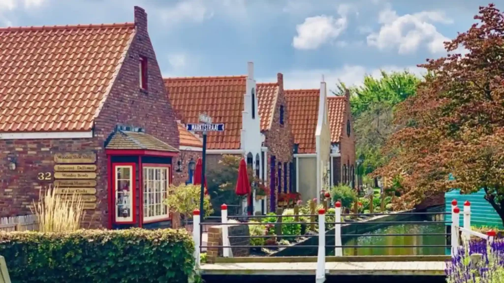 Scenic downtown Holland street with Dutch-style buildings, canal bridge, outdoor seating, and lush greenery in summer.