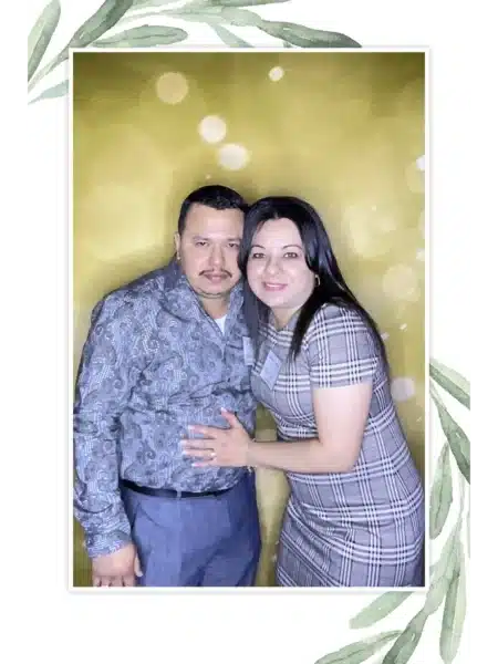 Two guests at a FastBooth photo booth posing in front of a glowing golden backdrop with leafy border