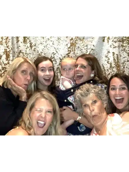 Six women and a baby posing playfully before a gold and white textured backdrop, captured by FastBooth in Michigan