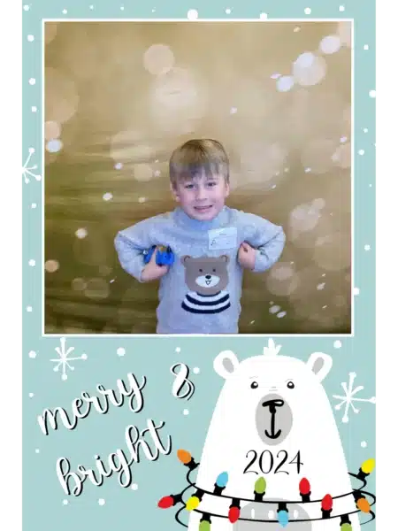 Child in a gray sweater holding a toy at a FastBooth photo booth with golden backdrop, snowflake border and merry & bright 2024 card