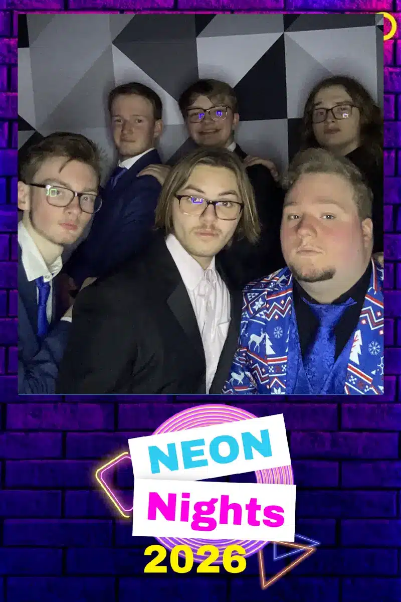 Six students in suits posing together at Neon Nights 2026 school dance photo booth in Michigan