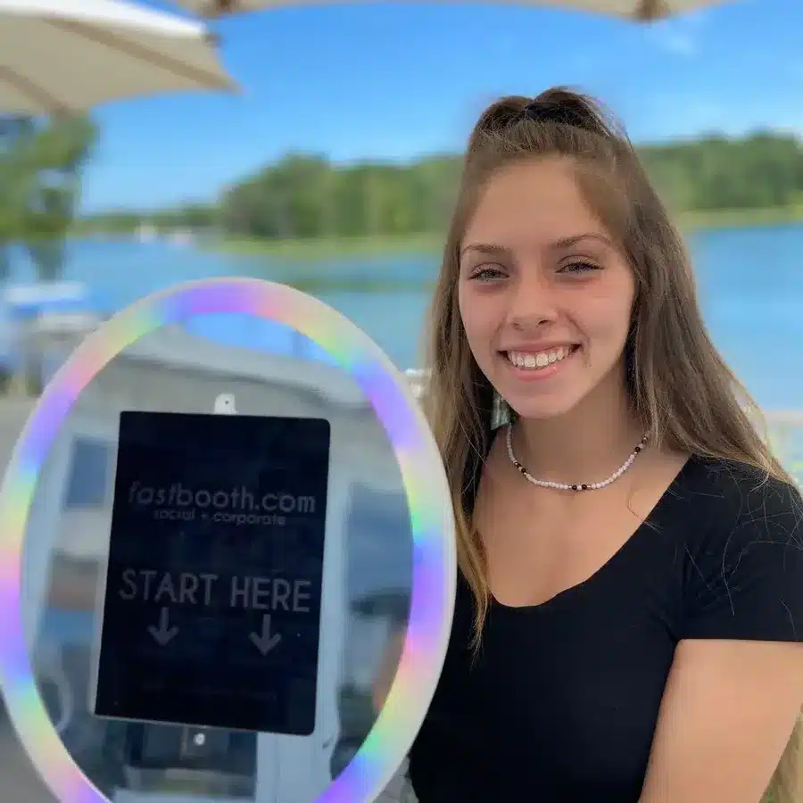 Smiling guest holding a FastBooth roaming ring-light photo booth with Start Here screen at an outdoor lakeside event